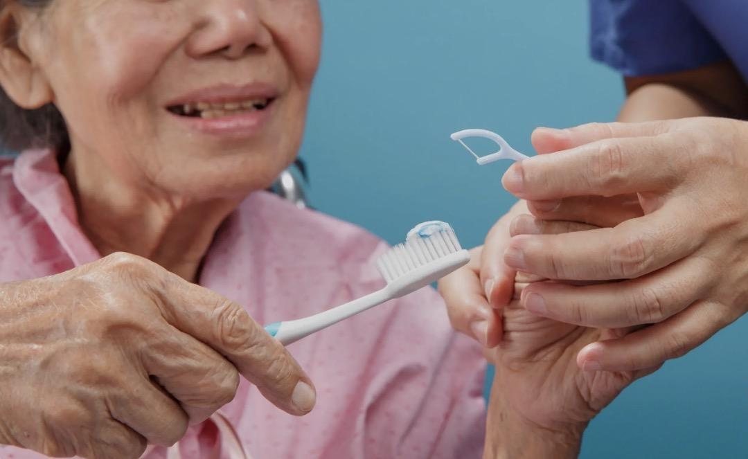 A caregiver helping an older patient brush her teeth.